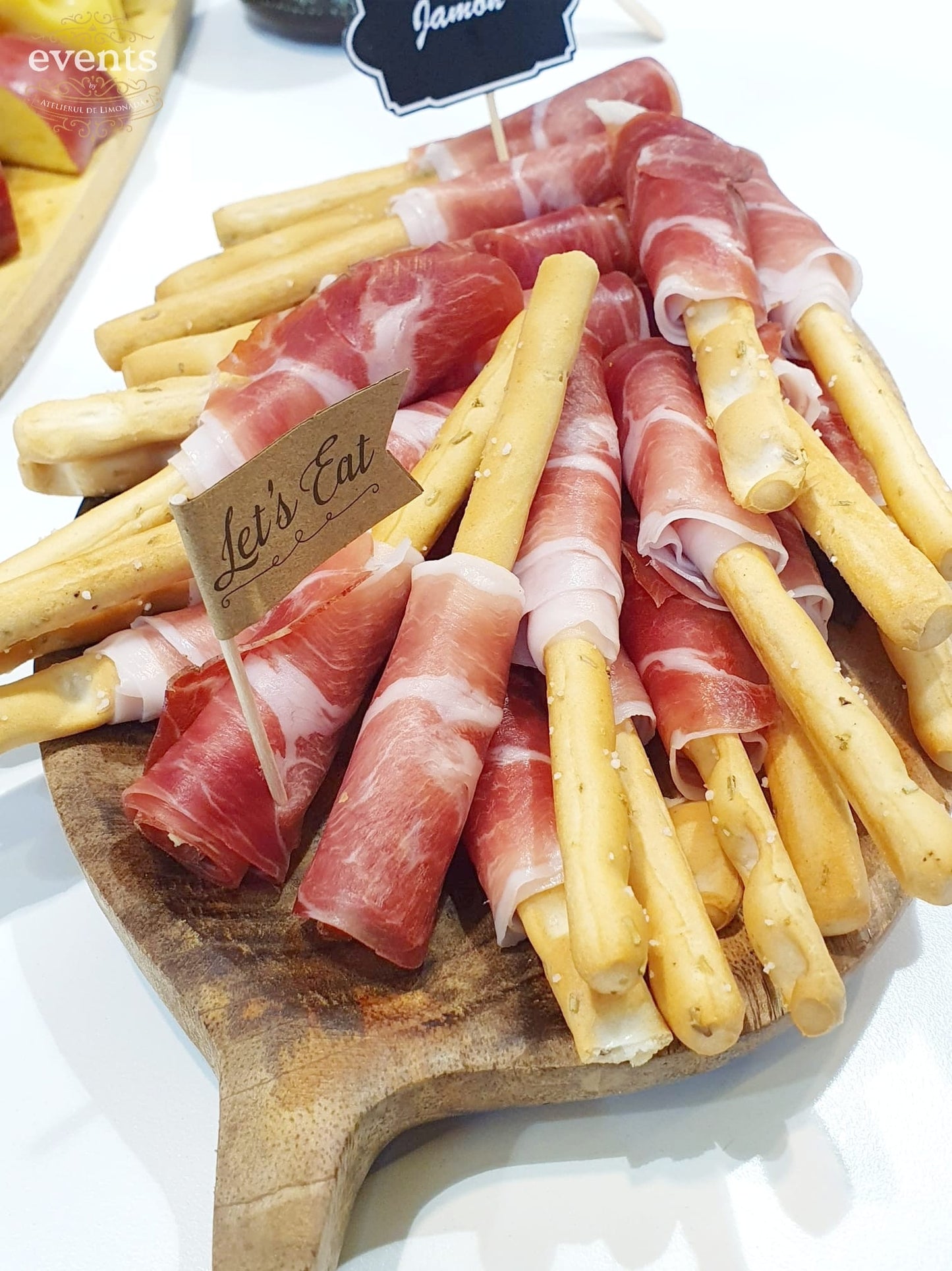 Grisine învelite în jamon (șuncă crud-uscată), servite pe un tocător de lemn ca parte dintr-un Cheese Bar pentru evenimente.