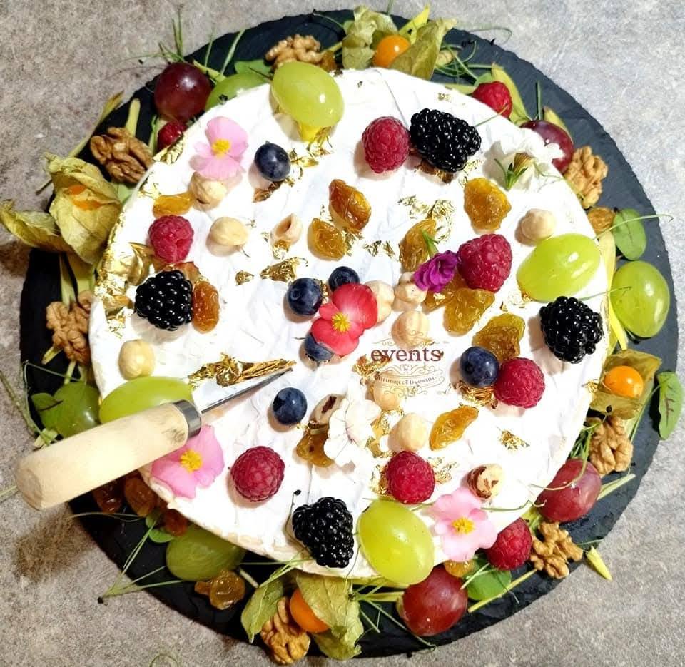 Rondea de brânză Brie decorată cu fructe de pădure, struguri, stafide aurii, flori comestibile, nuci și foiță de aur, parte dintr-un Cheese Bar gourmet.