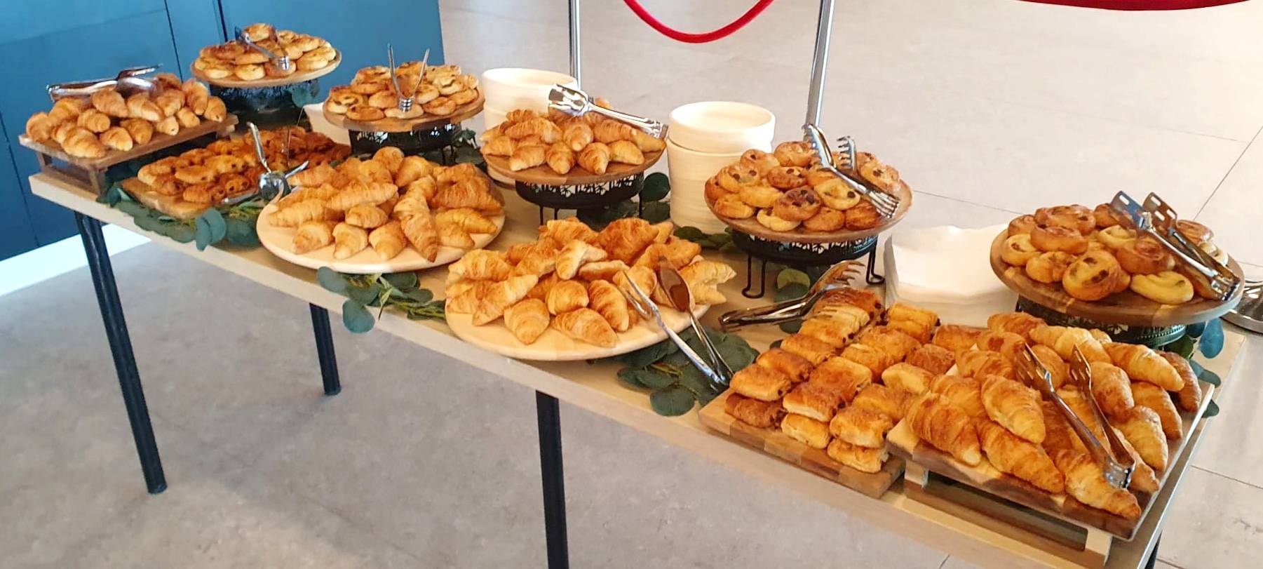 Bufet de patiserie proaspătă aranjat pentru o recepție corporate, cu o varietate de croissante și minipateuri asortate.