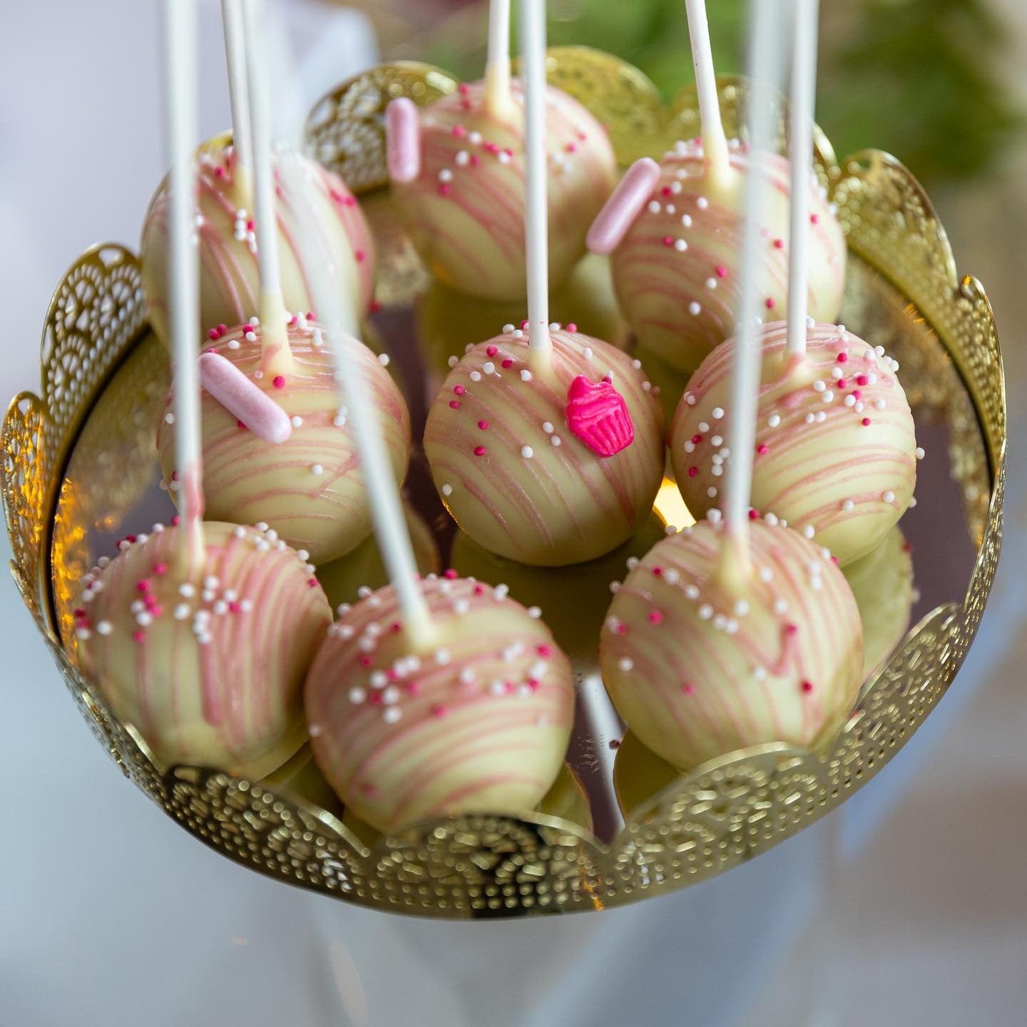 Cake pops glazurate în nuanțe de roz și alb, decorate cu bombonele, servite pe suport elegant la un candy bar pentru evenimente speciale – Atelierul de Limonadă.