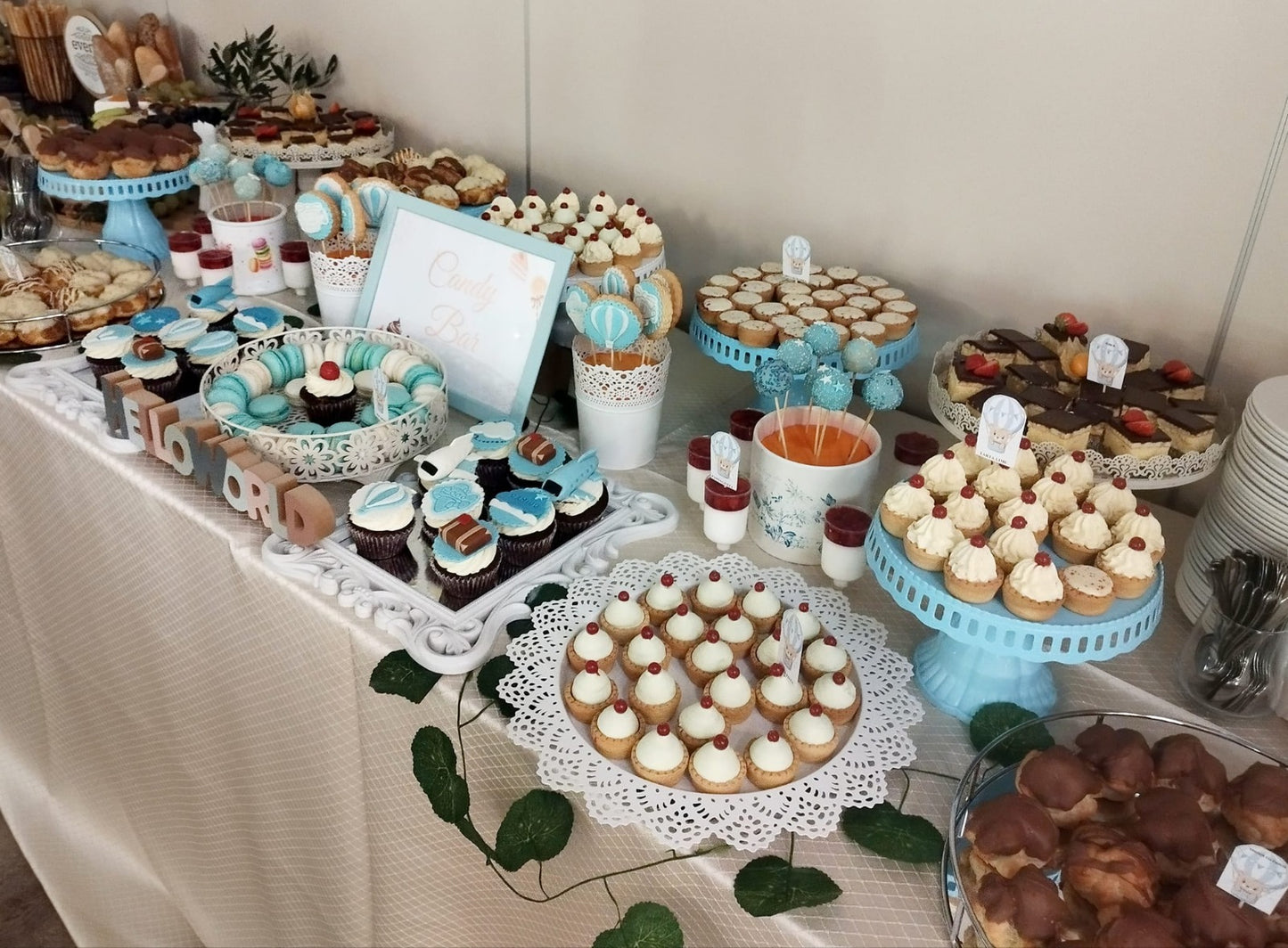 Candy bar elegant pentru botezul unui băiețel, decorat în nuanțe alb-albastru, cu macarons, cupcakes, cake pops și prăjituri fine – Atelierul de Limonadă.