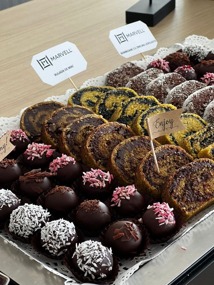 Rulade vegane cu mac și nucă, bomboane raw decorate cu fulgi de cocos, ciocolată și petale uscate, parte dintr-un Candy Bar vegan fără gluten, zahăr sau lactate, ideal pentru diete speciale și evenimente sustenabile.