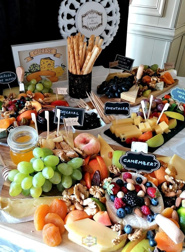 Cheese Bar cu brânzeturi variate etichetate – camembert, cașcaval, ementaler, gouda –, însoțite de fructe proaspete, miere, nuci, caise uscate și grisine.