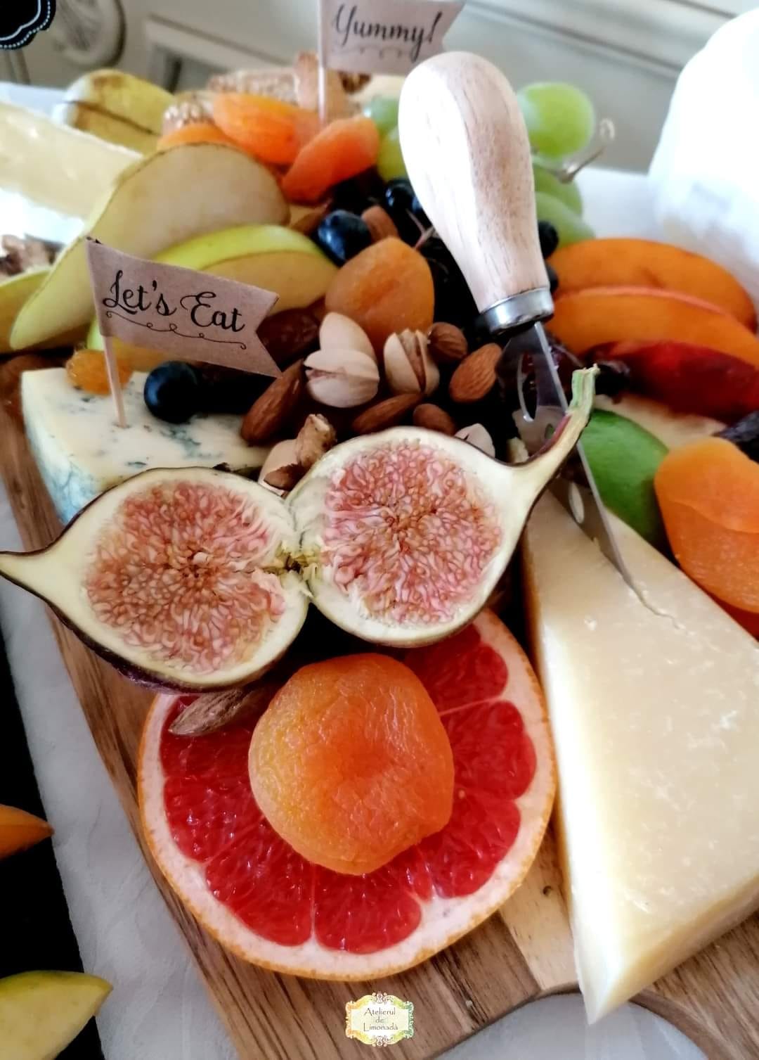 Prim-plan cu platou din Cheese Bar, cu brânză tare, smochine, grapefruit, caise uscate, pere, migdale, fistic, struguri și un cuțit de brânzeturi.