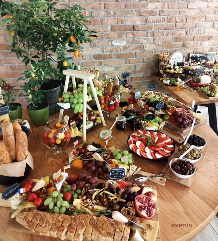 Cheese Bar în stil rustic, cu platouri variate de brânzeturi, pâine artizanală, struguri, nuci, legume, roșii cherry, măsline și decor natural cu plante în ghiveci.