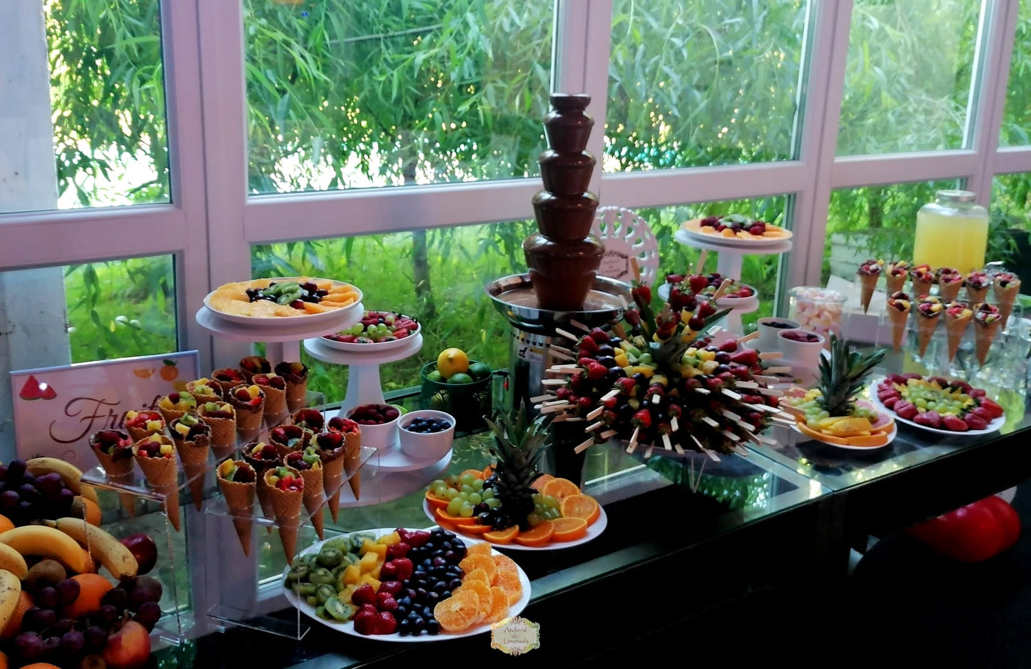 Fruit bar elegant cu fântână de ciocolată, conuri umplute cu fructe proaspete, frigărui din ananas și căpșuni și platouri bogate cu citrice, kiwi și struguri.