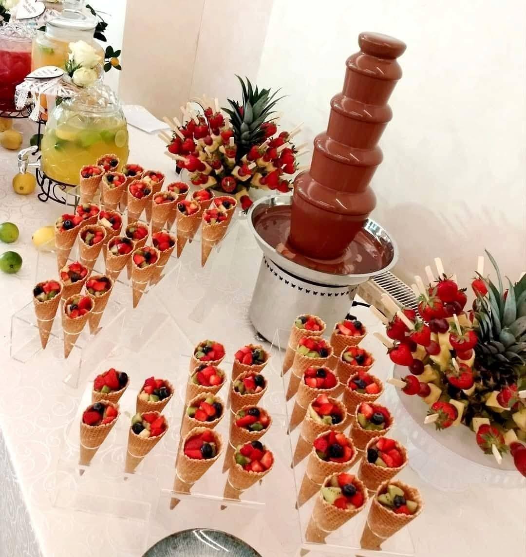 Conuri crocante umplute cu fructe proaspete, alături de fântână de ciocolată și aranjamente de ananas și căpșuni – parte din conceptul Fruit Bar by Atelierul de Limonada pentru evenimente rafinate.