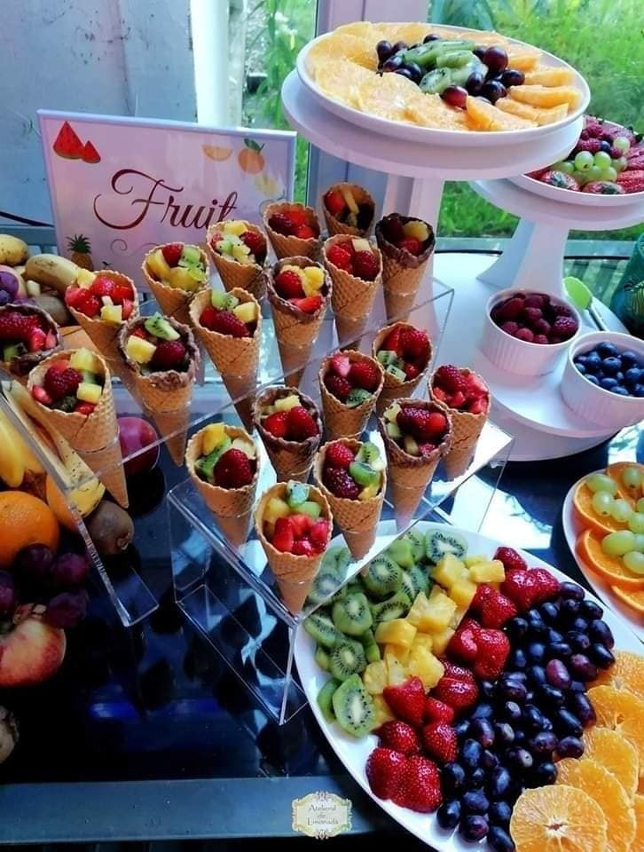 Conuri umplute cu fructe tropicale – kiwi, ananas, căpșuni – alături de platouri cu portocale, struguri și zmeură, expuse elegant într-un fruit bar pentru evenimente.