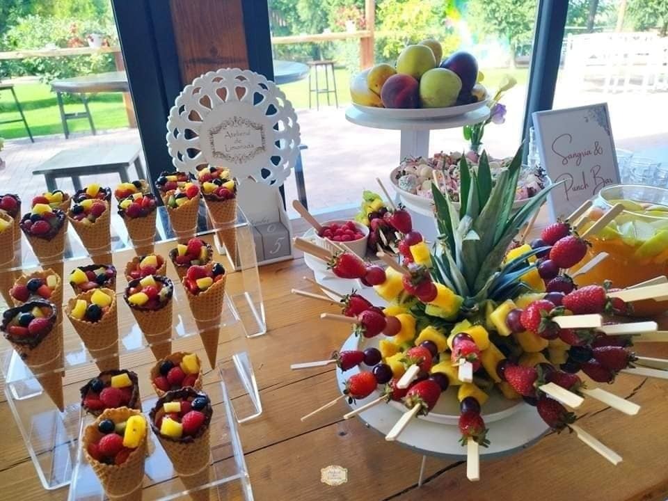 Conuri cu fructe glazurate și frigărui cu ananas, căpșuni și struguri, aranjate spectaculos într-un fruit bar cu decor tropical și fundal luminos.