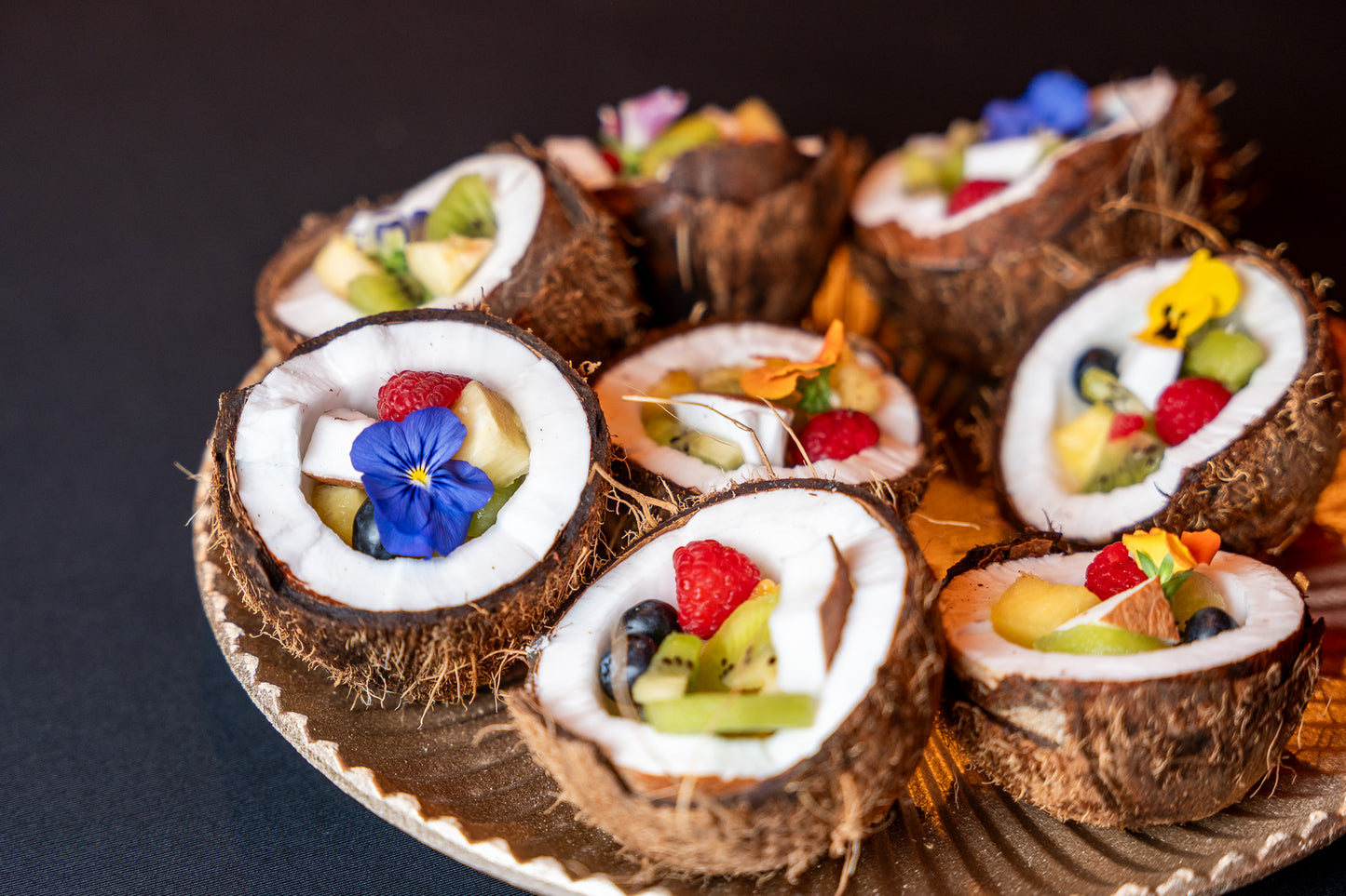 Fructe tropicale servite în jumătăți de cocos, decorate cu flori comestibile – o prezentare elegantă din conceptul Fruit Bar de la Atelierul de Limonadă.