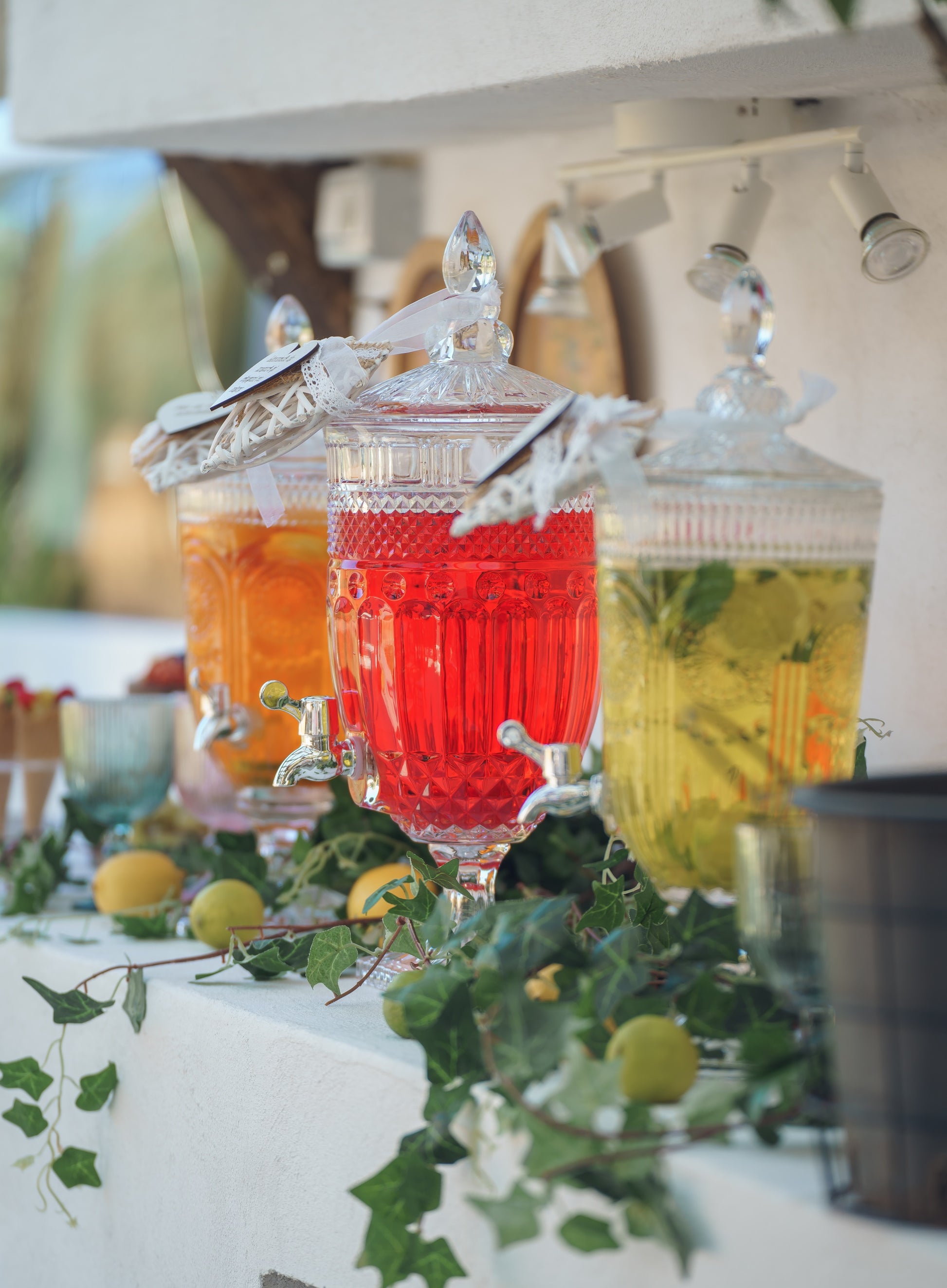 Stand de limonadă cu recipiente din cristal, decor cu lămâi și iederă, prezentând sortimente colorate de băuturi naturale pentru un eveniment elegant