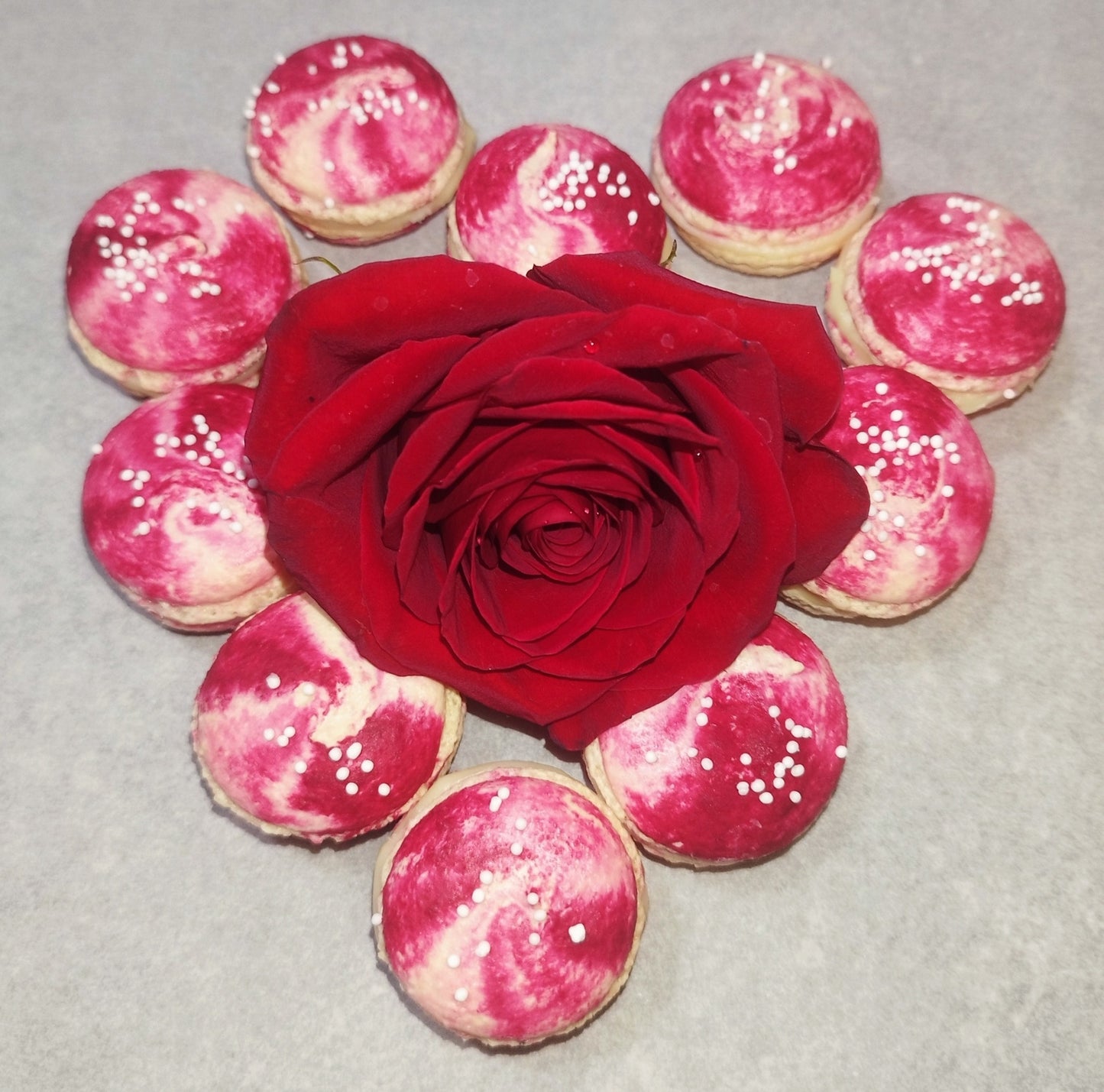 Macarons artizanali roz-alb, decorați cu perle de zahăr, aranjați în jurul unui trandafir roșu, cadoul perfect pentru Ziua Îndrăgostiților.