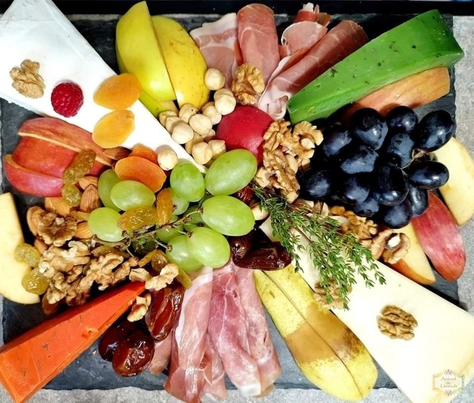 Platou cu brânzeturi variate, struguri, nuci, caise uscate, mere, pere, curmale, mezeluri fine și ierburi aromatice, parte dintr-un Cheese Bar pentru evenimente.