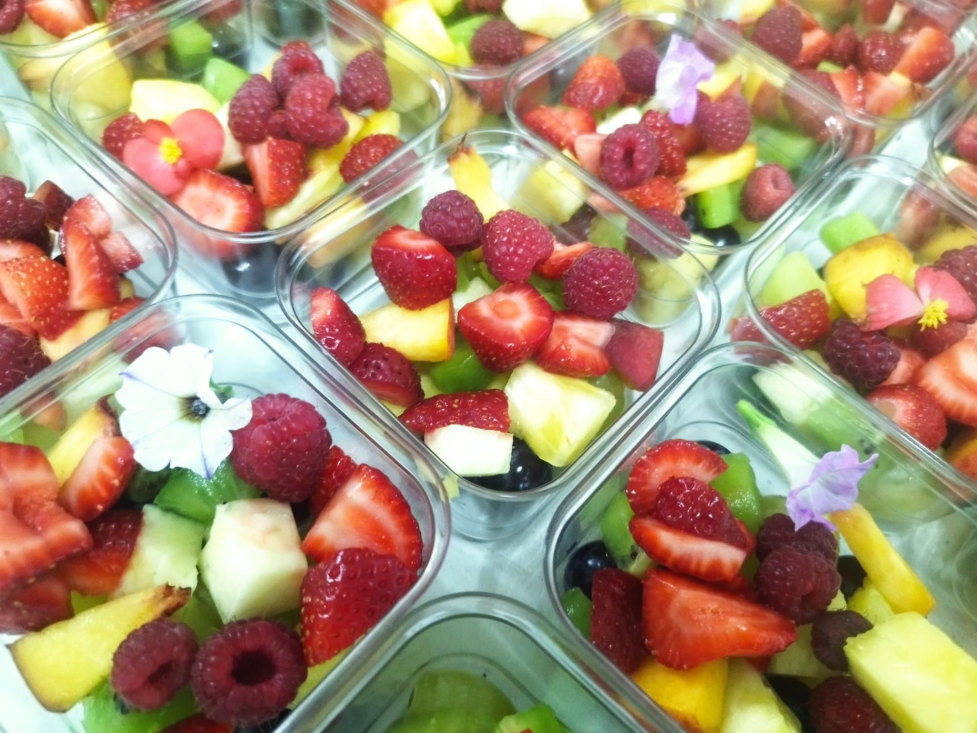 Close-up cu salate de fructe proaspete în caserole individuale pentru catering, cu căpșuni, zmeură, kiwi și flori comestibile.
