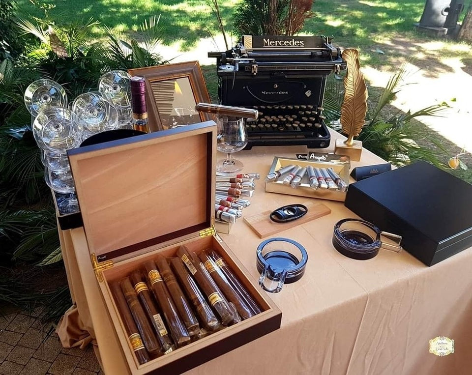 Amenajare elegantă Gentleman’s Corner în aer liber cu trabucuri premium, pahare de cognac, țigarete de foi și decor vintage cu mașină de scris.