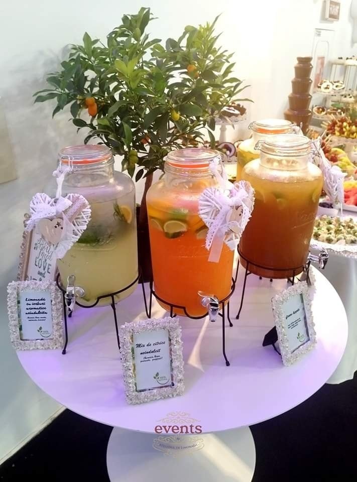 Stand de limonadă cu trei sortimente – limonadă cu mentă, mix de citrice și ghimbir – prezentate pe o masă rotundă decorativă la un eveniment.