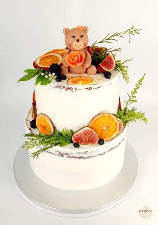 Tort personalizat tip naked cake cu două etaje, decorat cu fructe naturale (smochine, portocale, afine), verdeață și ursuleț din pastă de zahăr, ideal pentru botez sau baby shower.