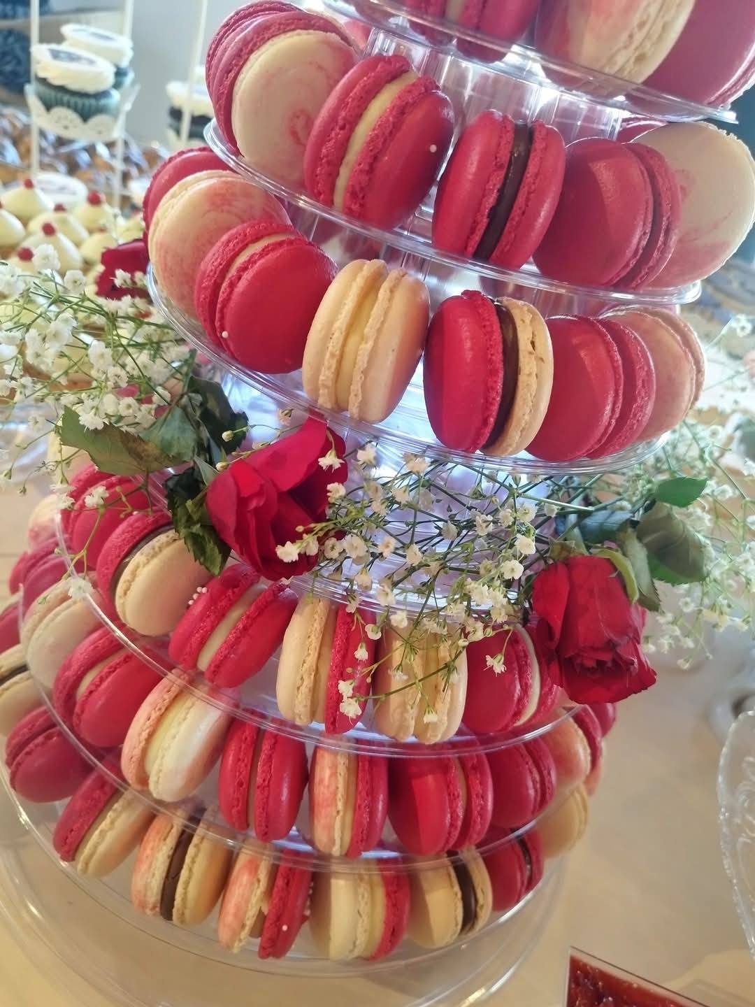 Turn de macarons roșii și crem pentru nuntă, decorat cu trandafiri, piesa centrală a unui candy bar elegant.