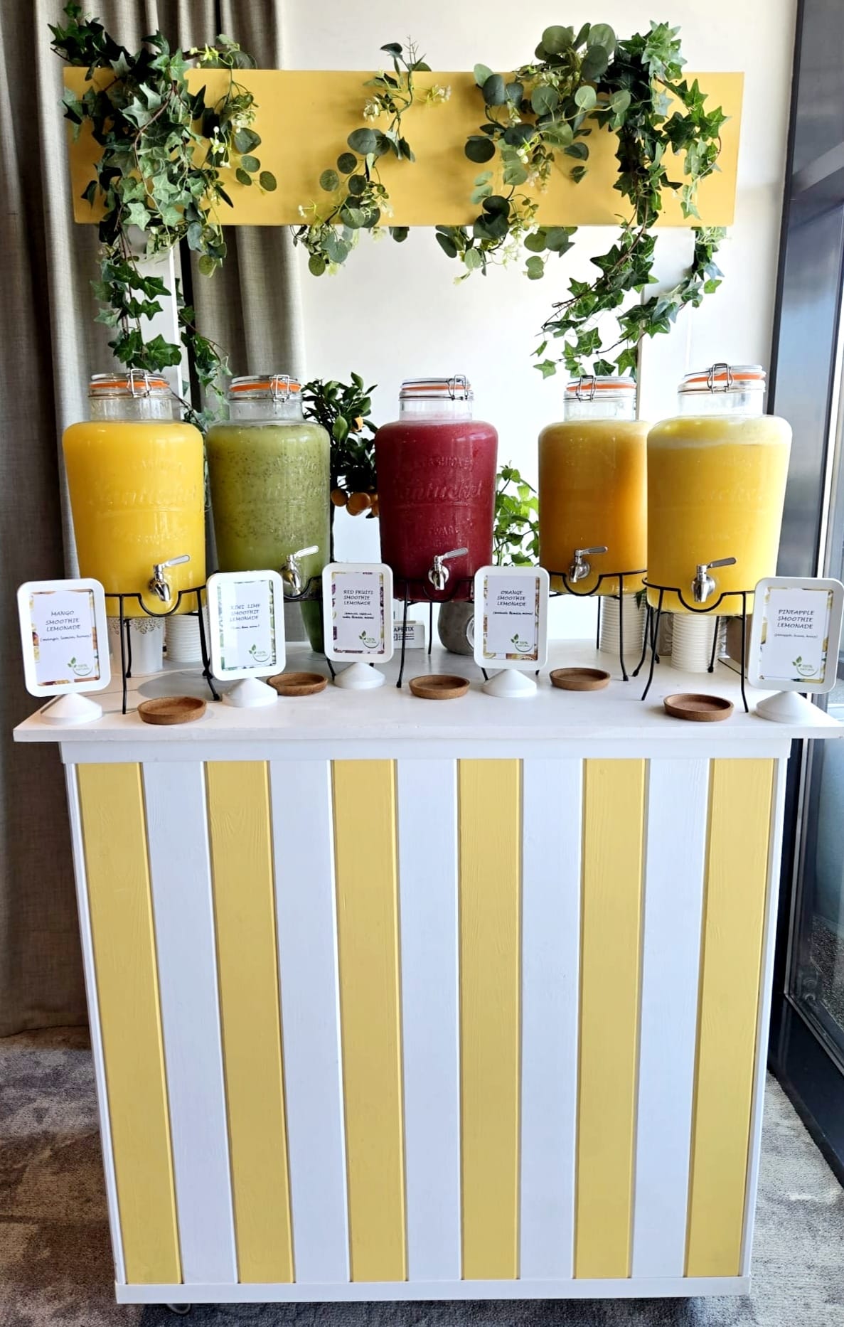 Bar mobil de smoothie, stand alb-galben, ideal pentru nuntă, botez sau evenimente corporate. Cinci sortimente de băuturi proaspete, inclusiv kiwi și fructe roșii. | Atelierul de Limonadă
