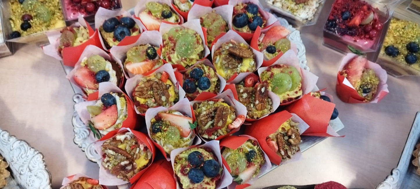 Platou cu brioșe vegane miniaturale, decorate cu afine, căpșuni, struguri și nuci pecan, prezentate în coșulețe de hârtie roșie pentru un candy bar.