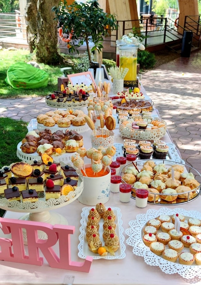 Candy bar de botez pentru fetiță, amplasat în grădină, decorat cu prăjituri, macarons și limonadă, marca Atelierul de Limonadă.