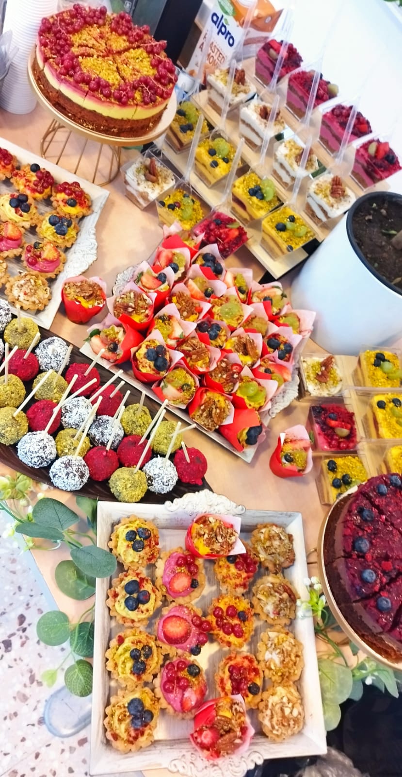 Vedere de sus a unui candy bar vegan bogat, cuprinzând torturi artizanale, mini tarte cu fructe, trufe și brioșe, aranjat profesional pentru un eveniment. By ateierul de limonada.