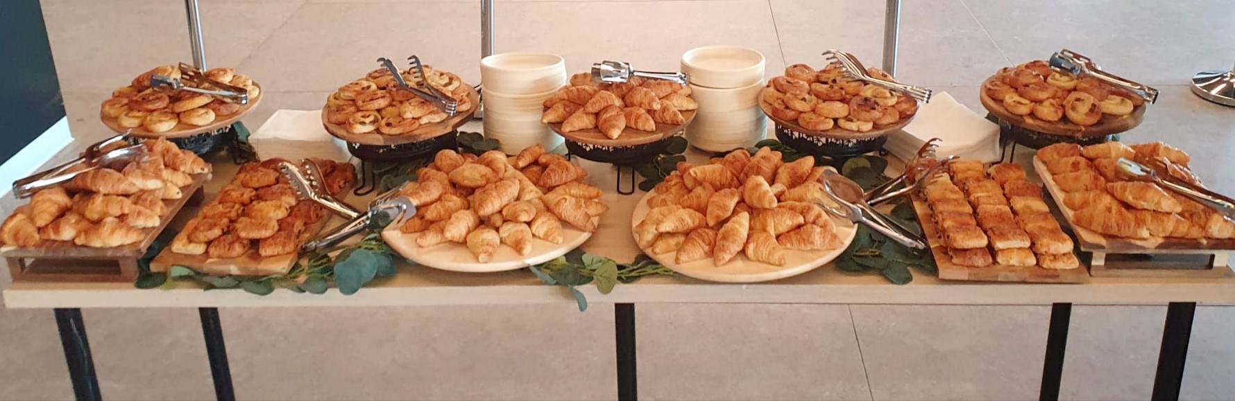Bufet de patiserie pentru pauza de cafea la o conferință, cu platouri bogate de minicroissante și melci cu stafide.
