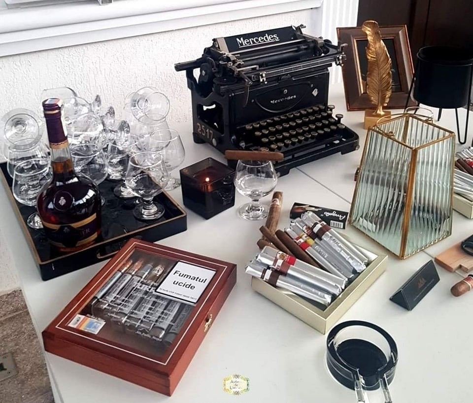Colț elegant de gentleman cu trabucuri premium, cognac fin, pahare de degustare și decor vintage cu mașină de scris și obiecte de colecție.