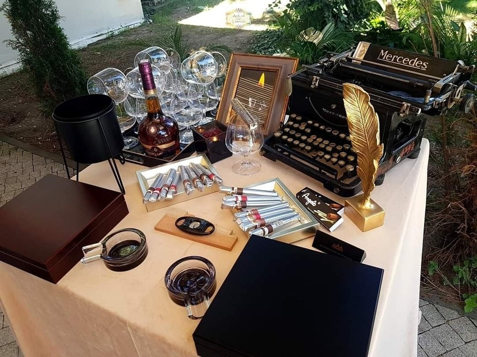 Setup elegant cu trabucuri ambalate individual, cognac fin, pahare de degustare, mașină de scris vintage și decorațiuni aurii pentru un gentleman's corner rafinat.