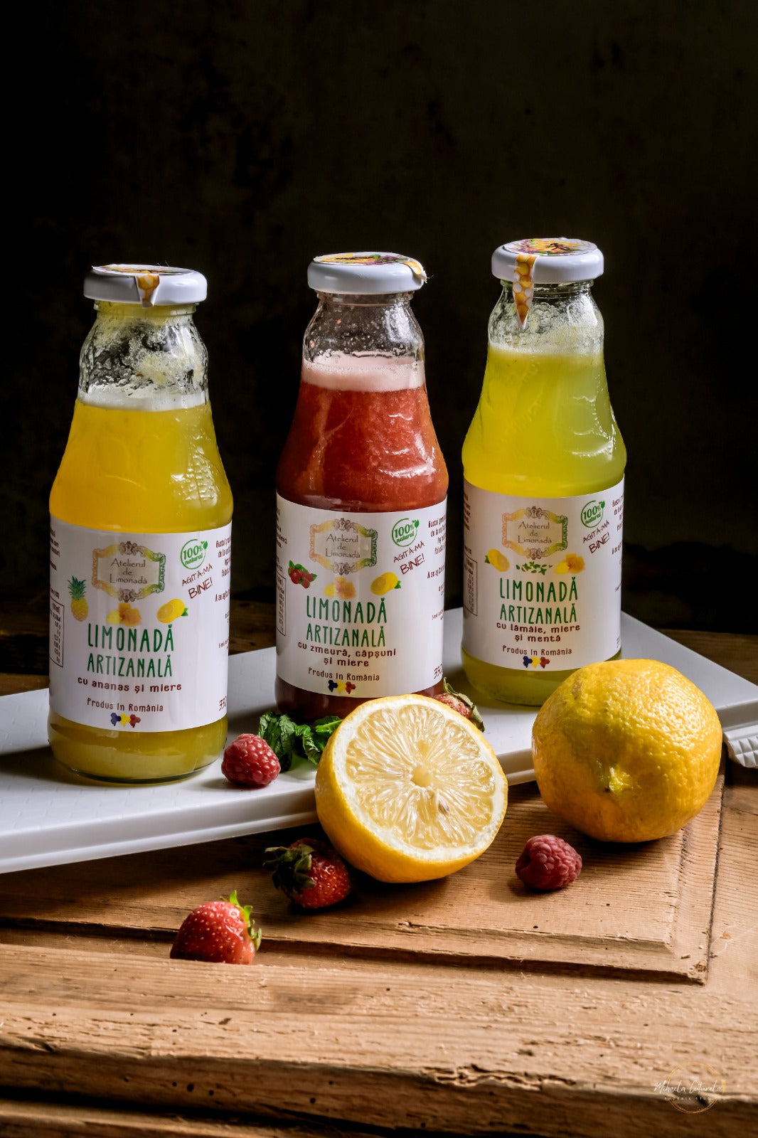 Trei sortimente de limonadă artizanală la sticlă – cu ananas, zmeură și lămâie – alături de fructe proaspete.