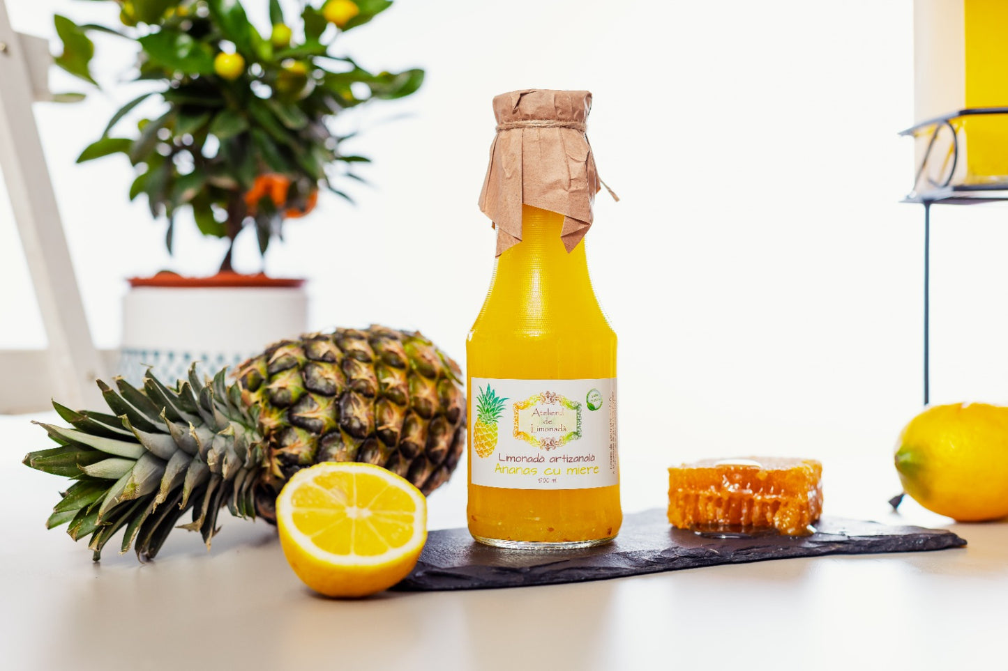 Sticlă de limonadă la sticlă cu ananas și miere, alături de ananas proaspăt, lămâie și fagure natural, pe fundal alb decorativ.