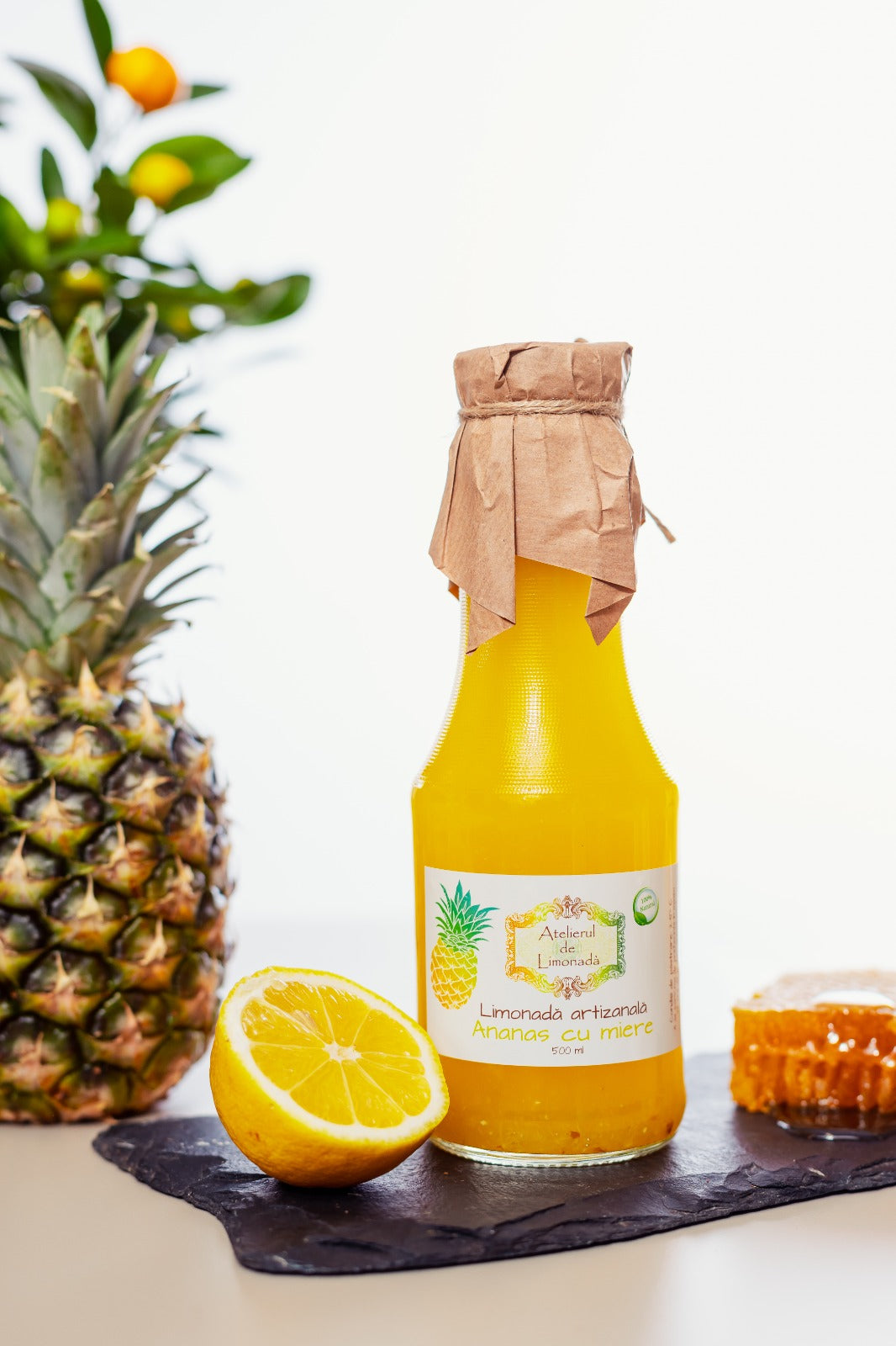 Prim-plan cu sticlă de limonadă la sticlă cu ananas și miere, alături de ananas, lămâie proaspătă și fagure natural, pe fundal alb.