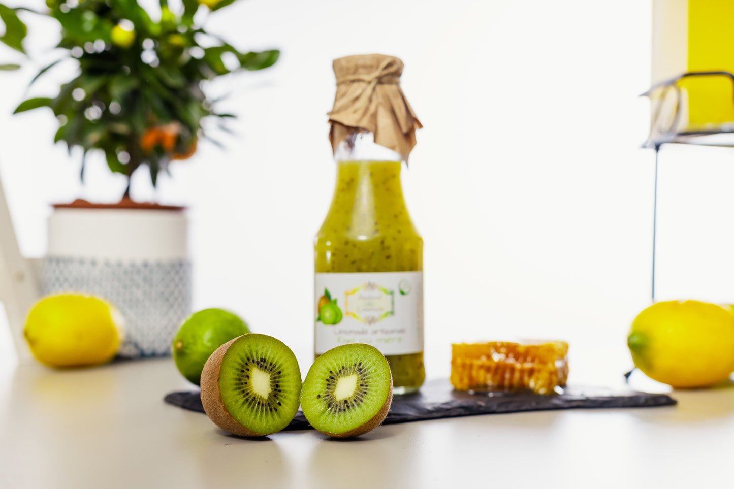 Sticlă de limonadă la sticlă cu kiwi și miere, evidențiată de fructe proaspete de kiwi, lămâi, lime și fagure natural, pe fundal alb.