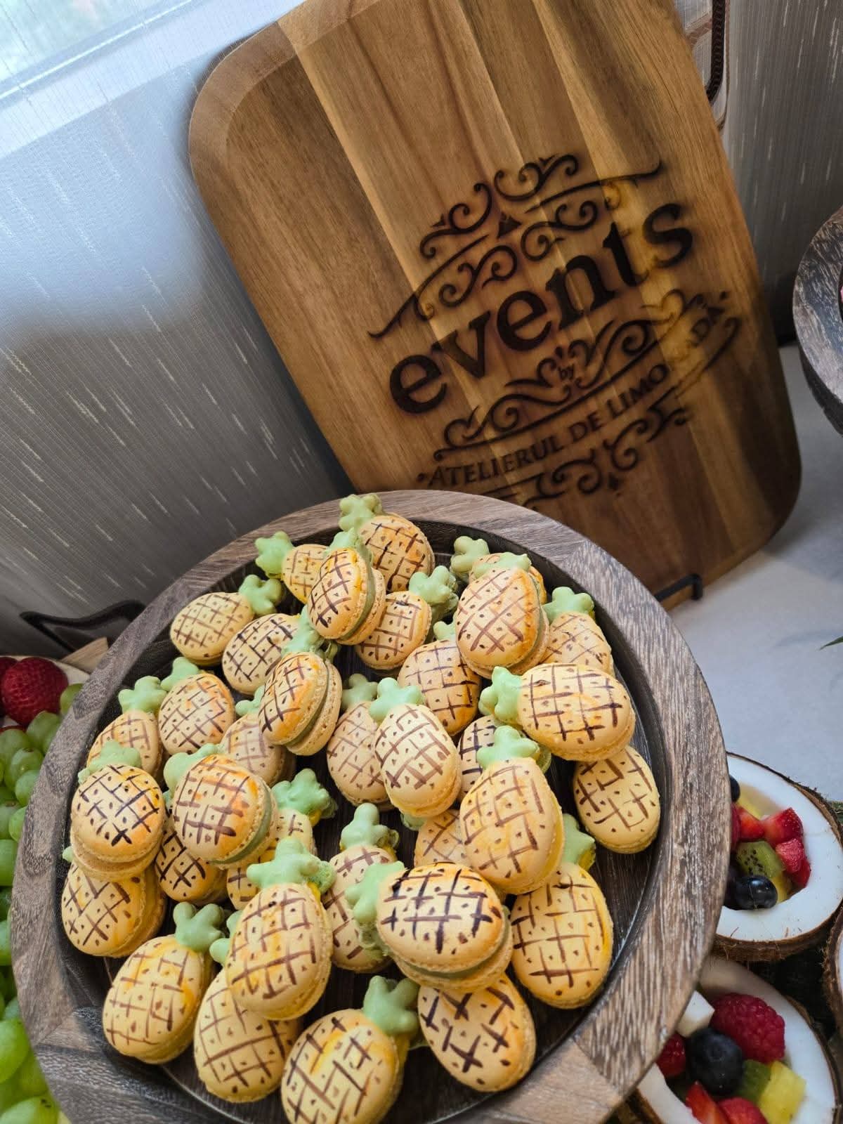 Macarons în formă de ananas serviți pe un platou de lemn, deserturi perfecte pentru o petrecere corporate, nunta sau botez.