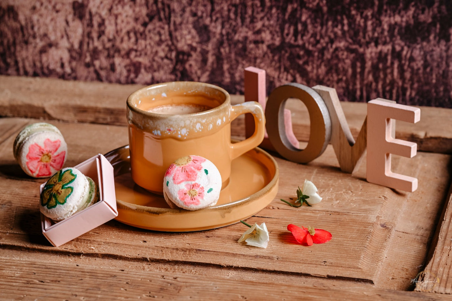 Macarons artizanali pictați manual cu flori, un cadou romantic lângă o ceașcă de cafea și semnul "LOVE"