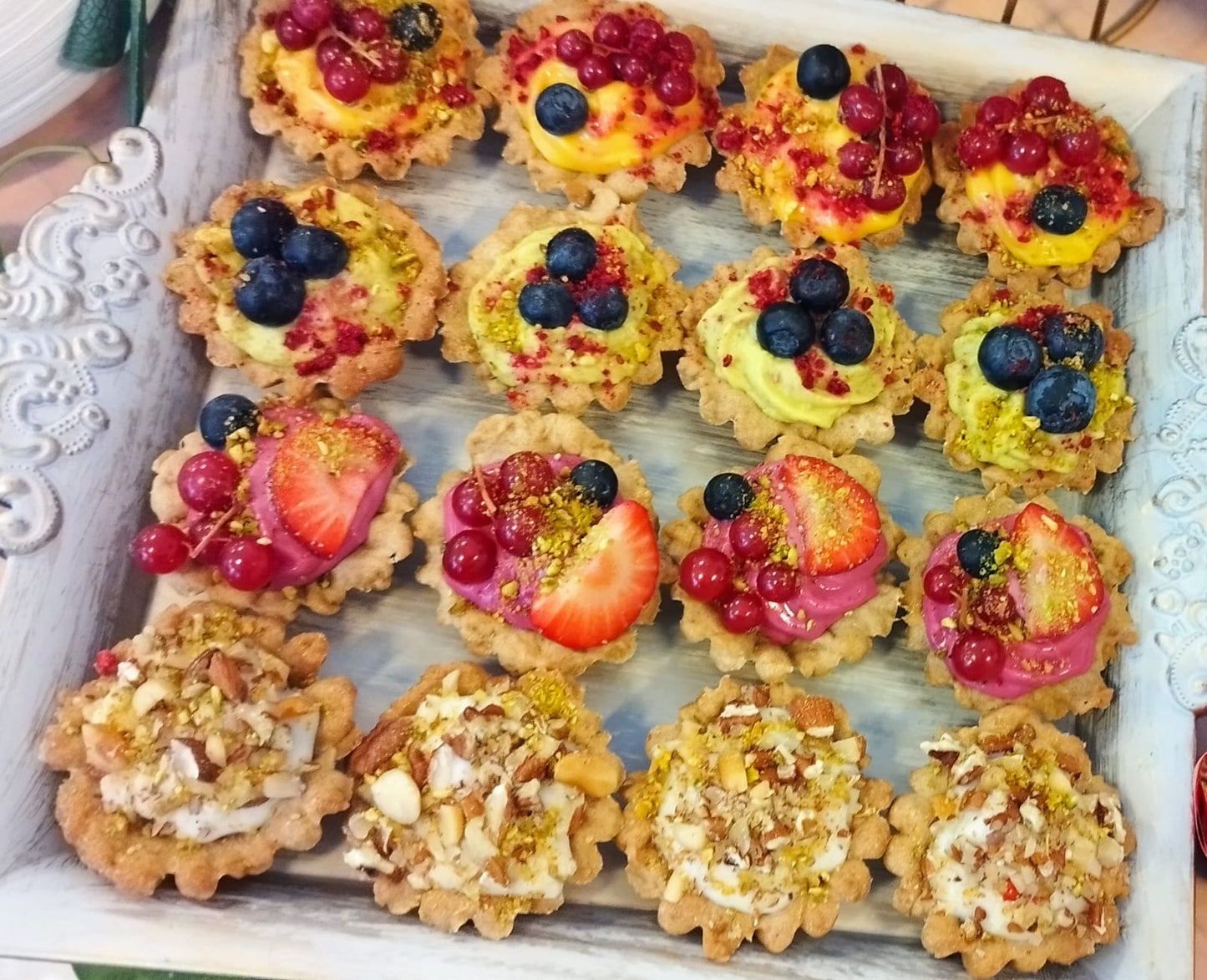 Platou cu mini tarte vegane asortate, decorate cu afine, coacăze, căpșuni și nuci, ideale pentru un candy bar sănătos la evenimente.