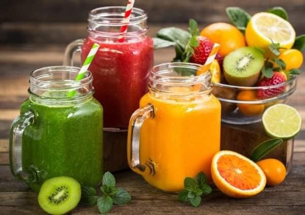 Smoothie-uri naturale servite în borcane – kiwi, portocale, fructe de pădure și lime, înconjurate de fructe proaspete.