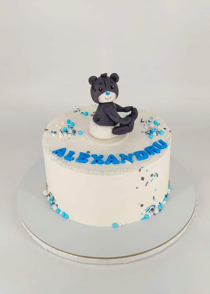 Tort de botez pentru băieței, cu glazură albă, personalizat cu numele Alexandru și decorat cu un ursuleț gri din pastă de zahăr.