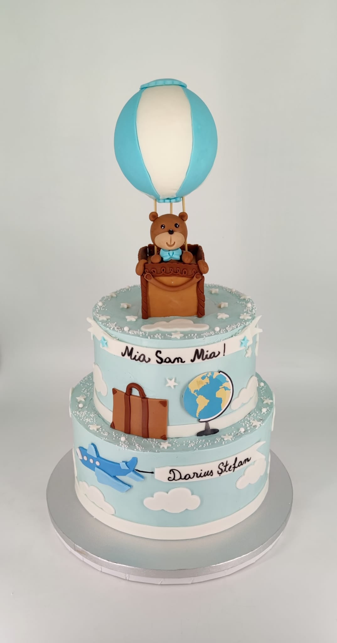 Tort de botez etajat pentru băieței, cu tematica călătorie, personalizat cu numele Darius Ștefan și decorat cu balon cu aer cald, ursuleț, avion și glob pământesc.