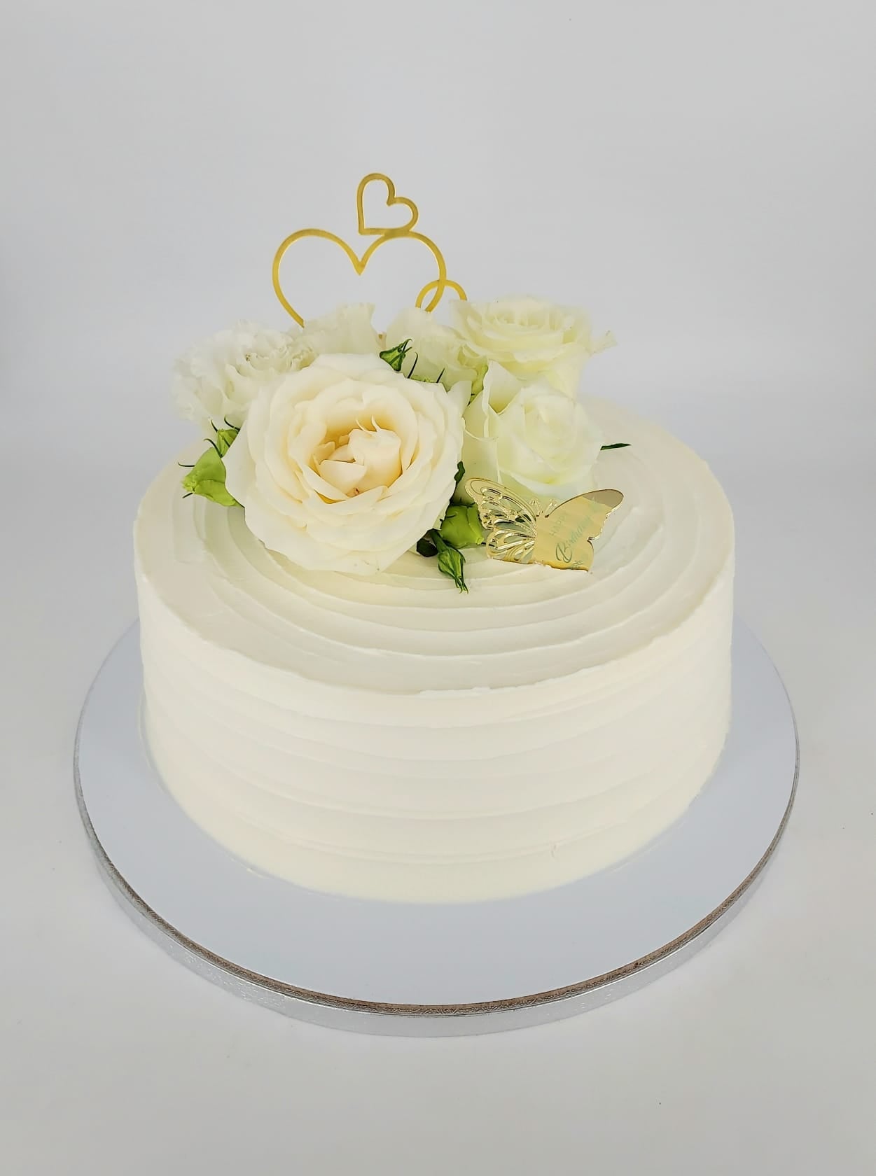 Tort alb minimalist pentru cununie civilă, cu frișcă texturată, decorat cu trandafiri crem naturali, un fluture auriu și un topper cu inimioare.