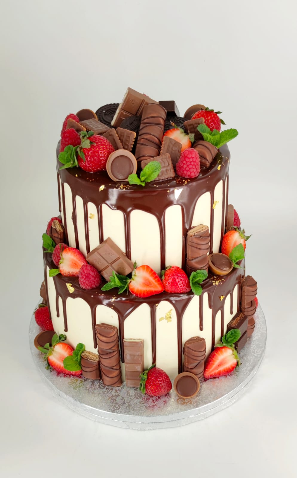 Tort etajat de tip drip cake, cu glazură de ciocolată, decorat abundent cu Kinder Bueno, Oreo, căpșuni proaspete și zmeură.