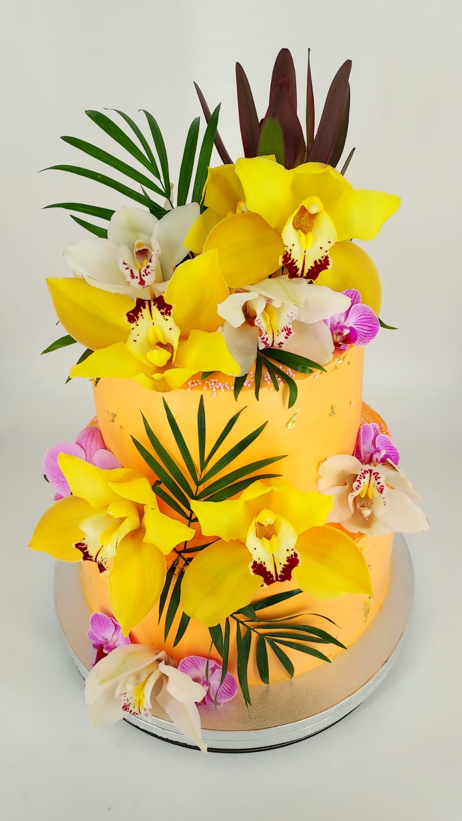 Tort portocaliu etajat, pentru evenimente speciale, decorat cu un aranjament bogat de orhidee naturale galbene și albe.