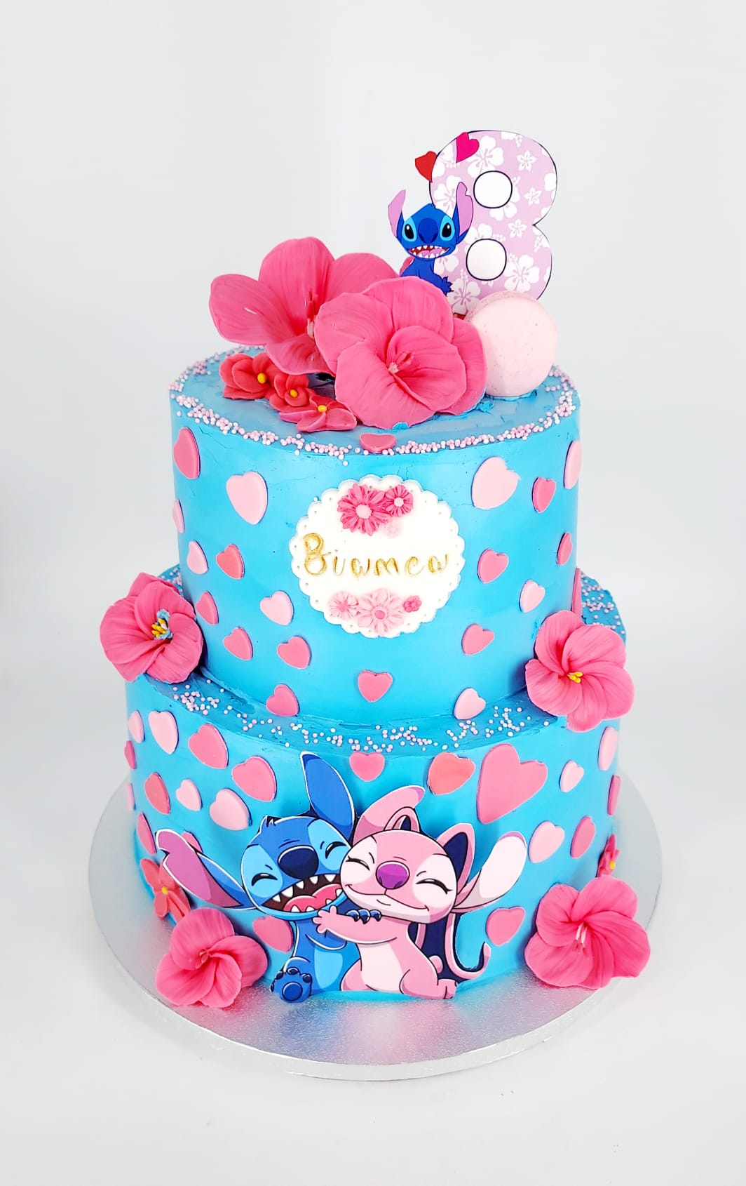 Tort de aniversare pentru fetițe, cu două etaje, tematică Lilo și Stitch, ornat cu figurinele Stitch și Angel, flori roz de hibiscus și cifra 8.