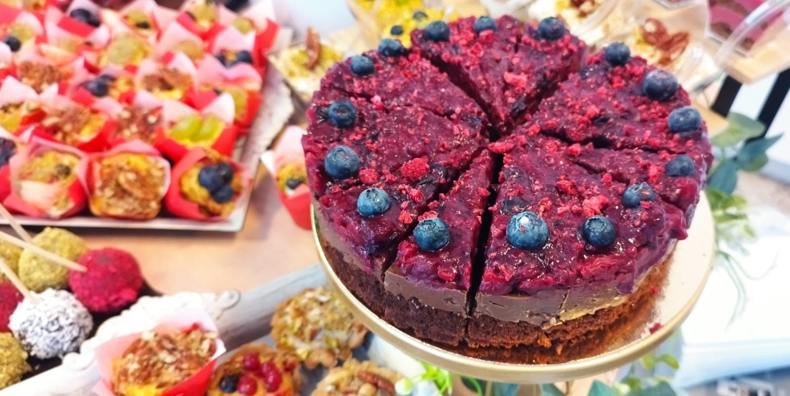 Plan apropiat cu un tort vegan cu bază de ciocolată și glazură de afine, înconjurat de brioșe și trufe raw-vegane la un bufet de deserturi. Atelierul de limonada.