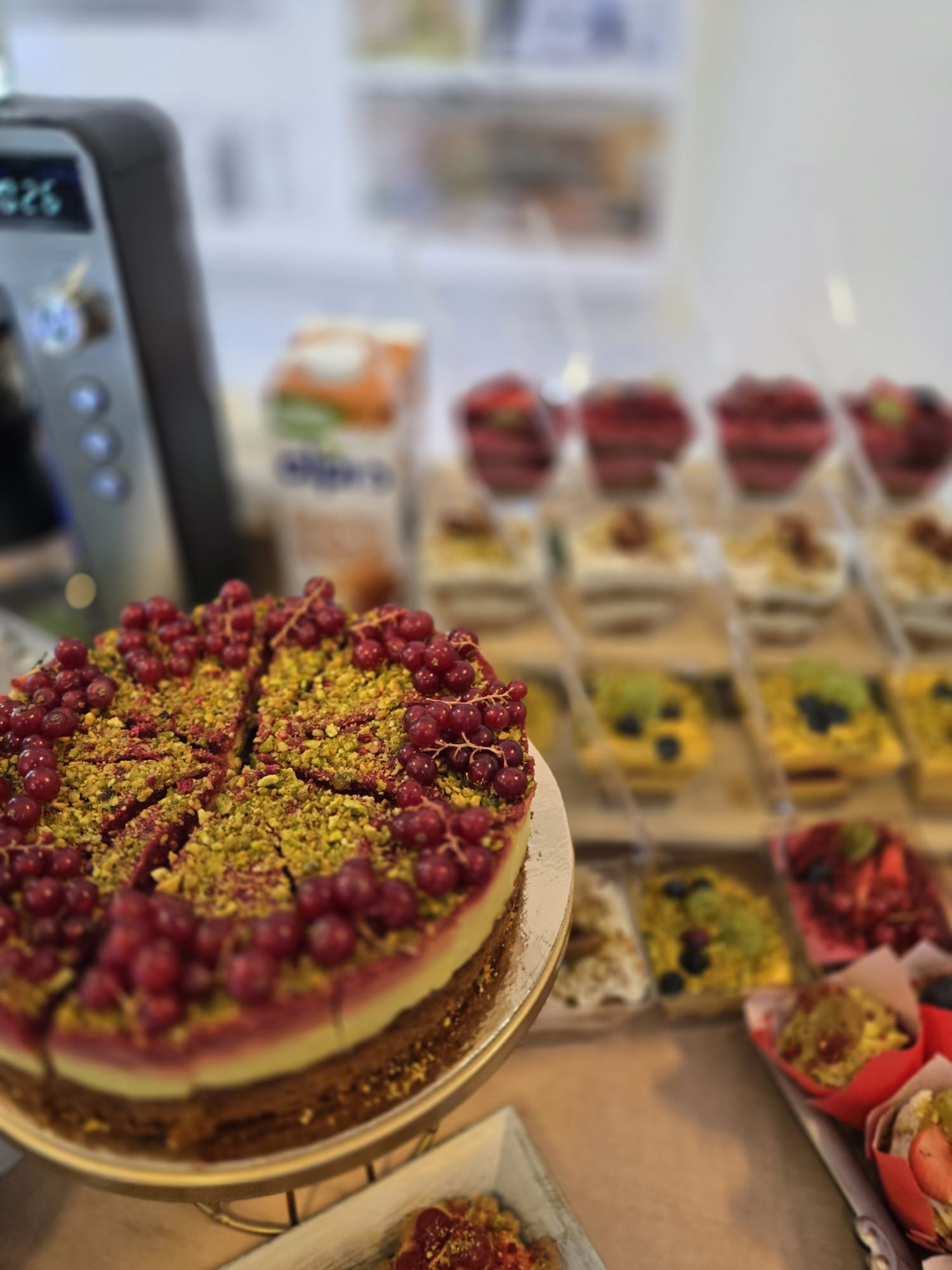 Imagine de ansamblu cu un tort vegan decorat cu fistic și coacăze roșii, înconjurat de o varietate de mini-deserturi sănătoase la un candy bar pentru evenimente.