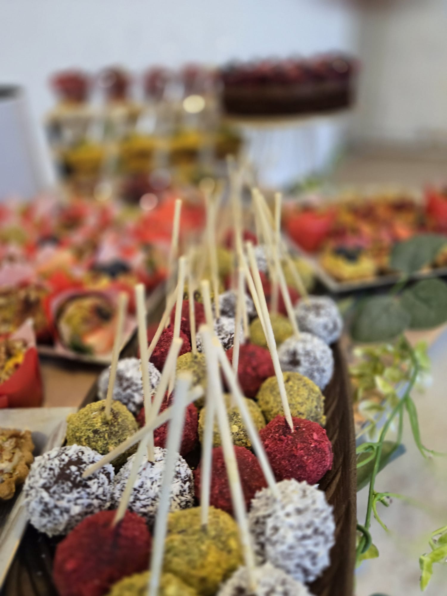 O selecție de trufe raw-vegane pe băț, colorate natural cu nucă de cocos și fistic, prezentate la un candy bar pentru evenimente. By Ateleirul de limonada.