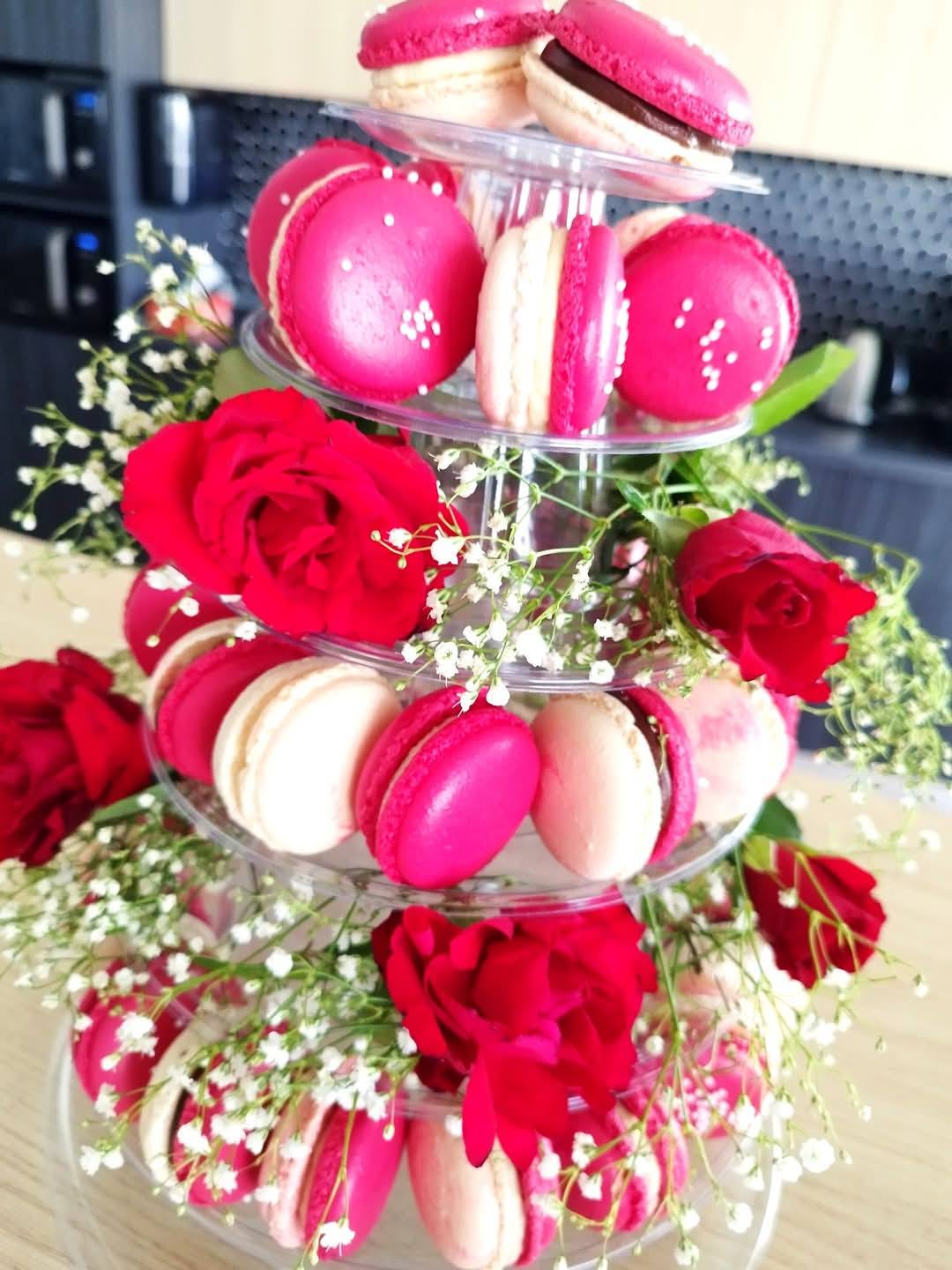 Turn de macarons roz fuchsia și crem, decorat cu trandafiri roșii și gypsophila, ideal pentru candy bar-ul unei nunți.